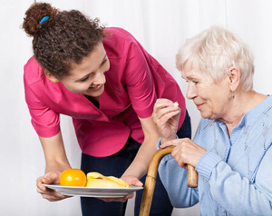 Bildinhalt: eine junge Frau bietet einer älteren Frau Obst an